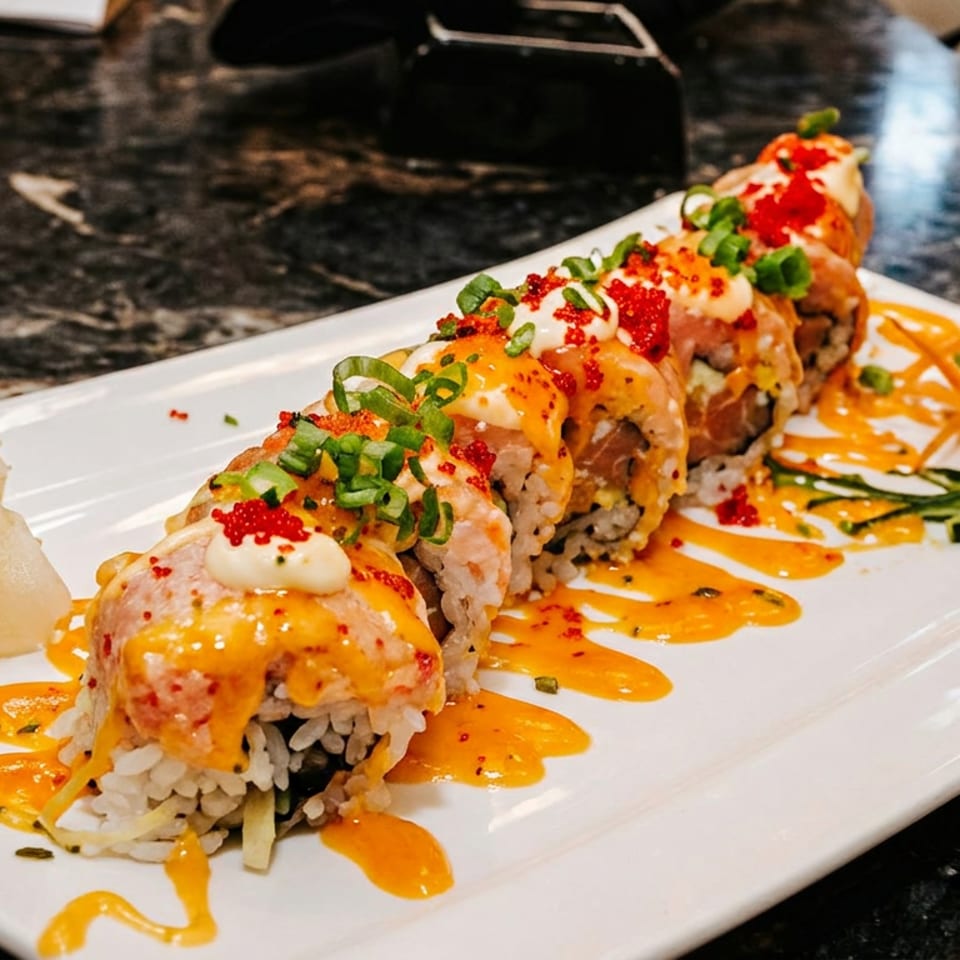 Sushi roll with spicy sauce, green onions, and roe, served with ginger and wasabi.